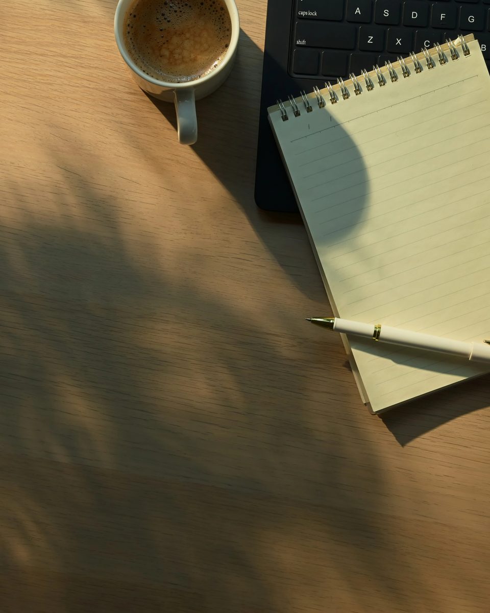 A notebook and pen on a wooden desk in leaf shadows